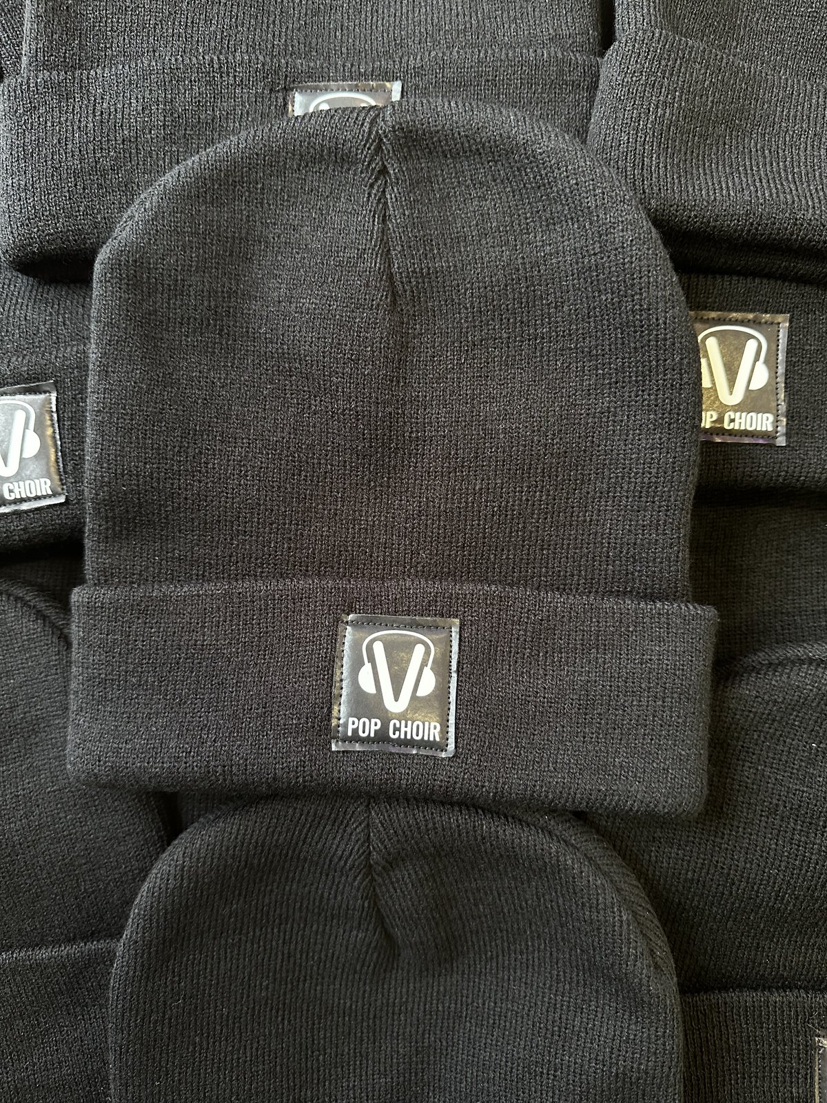 Pop Choir embroidered caps by Melbourne Merch - strong repetition and texture in this real-world massed product shot, clear focus on custom labels